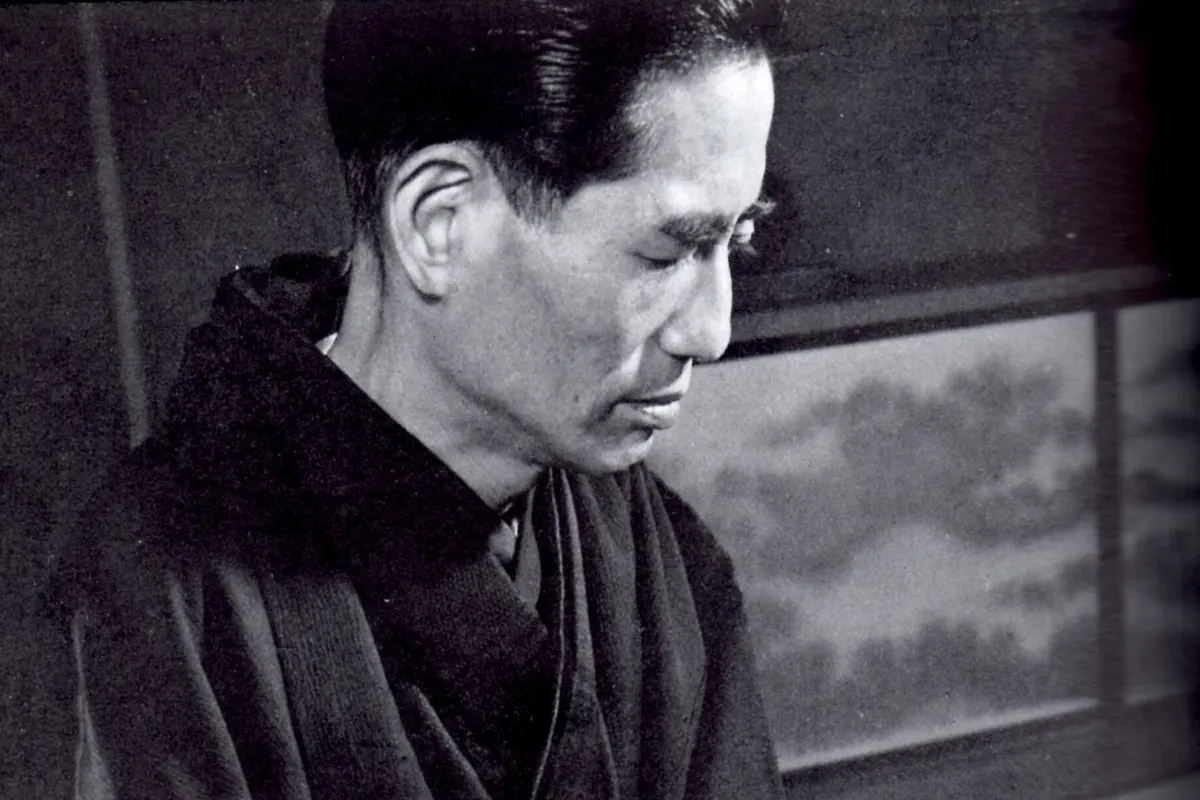 Černobílý portrét skladatele Mičia Mijagiho v kimonu, se sklopenýma očima, sedícího u svého koto