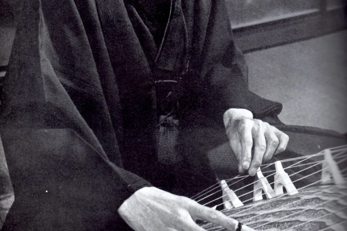 Primer plano de la mano derecha de un intérprete de koto con púas en los dedos junto a los puentes móviles, de una fotografía en blanco y negro de Michio Miyagi